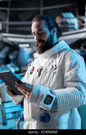 Astronaut researcher calibrating spacecraft sensors using tablet, carrying out research. Scientist wearing cosmonaut gear in spaceship conducting safety checks during flight Stock Photo