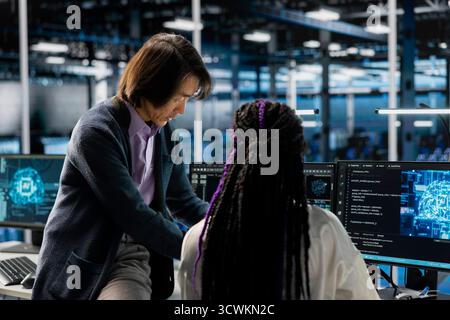 Senior programmer and trainee coding in diverse data center, updating AI automation scripts. Server room manager and intern programming artificial intelligence algorithms Stock Photo