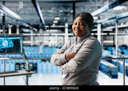 Portrait of smiling data center technician tasked with reviewing code for AI automation scripts. Happy african american woman in server hub running artificial intelligence assisted diagnostics on gear Stock Photo