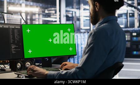 Data center technician doing software updates using green screen mockup computer. Server room IT specialist , optimizing infrastructure using chroma key isolated screen PC, camera A Stock Photo