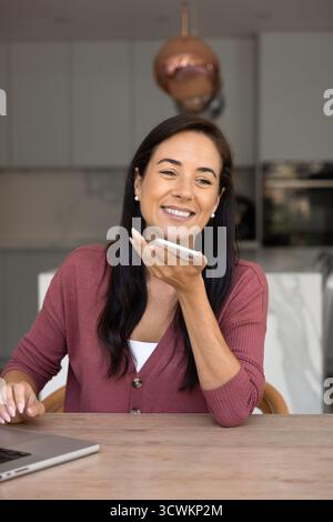 Positive Hispanic freelance worker woman talking on speaker on cellphone Stock Photo