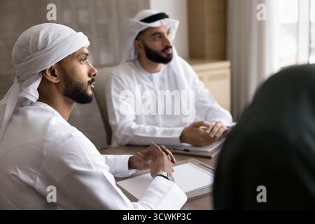Young Arab businessmen wear Muslim dress sit by conference table Stock Photo