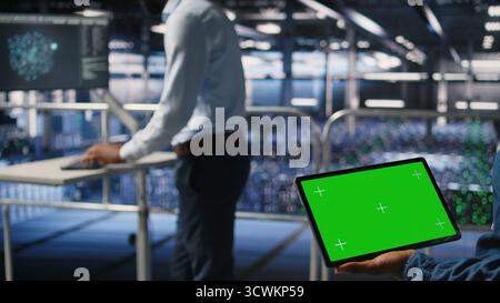 Server hub engineers finetuning configurations using chroma key device. Close up of technicians on data center industrial platform analyzing performance outputs on isolated screen tablet, Stock Photo