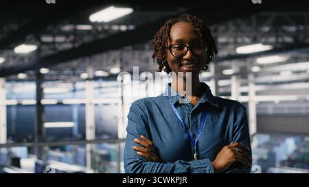 Portrait of smiling data center admin next to coworkers running diagnostics on equipment to identify errors. Happy woman next to IT experts working to prevent failure and minimize downtime Stock Photo
