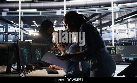 System administration team collaborating on AI automation deployment in data center. Server farm staff members adjusting machine learning configurations, working together, camera A Stock Photo