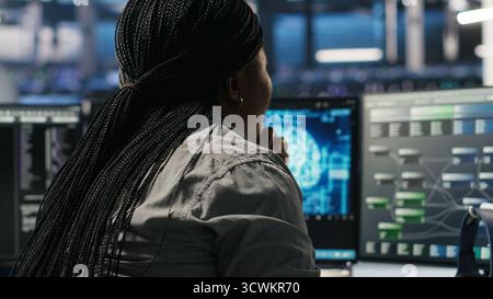 Data center software developer using artificial intelligence deep learning models to configure hardware. IT professional works on AI programming language in server farm, optimizing system, camera B Stock Photo