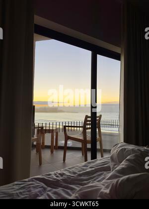 View from a cozy bed looking out to a serene hotel balcony with chairs and table at sunrise over a scenic ocean horizon Tenerife Canaries Stock Photo