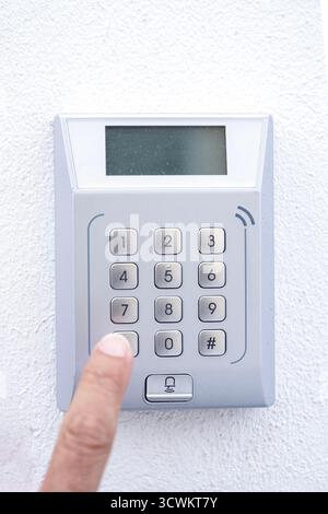Close-up of ahand pressing a button on a numeric keypad for a security system or entry doo, the panel is mounted on a white wall Stock Photo