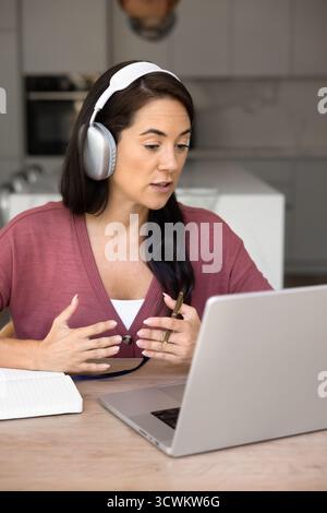 Serious Latin online teacher woman in wireless headphones giving webinar Stock Photo