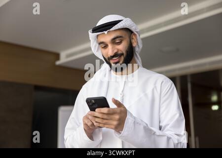 Smiling young middle eastern businessman hold smartphone read message text Stock Photo