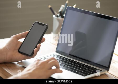 Closeup young man entrepreneur using notebook smartphone at workplace desk Stock Photo