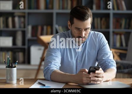 Serious young man business professional sitting at desk using smartphone Stock Photo