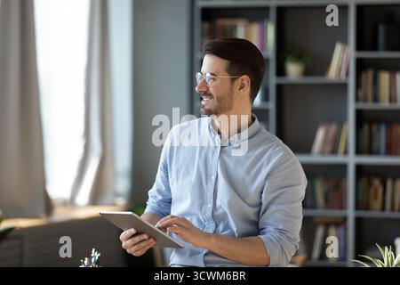 Cheerful young entrepreneur holding tablet pc looking aside from screen Stock Photo