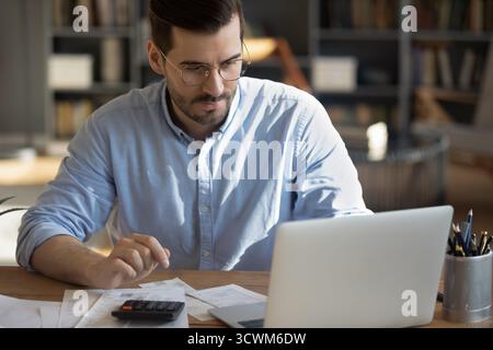Millennial businessman paying bills online via bank app on notebook Stock Photo