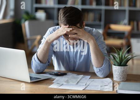 Frustrated young man grabbing head in despair checking finance documents Stock Photo