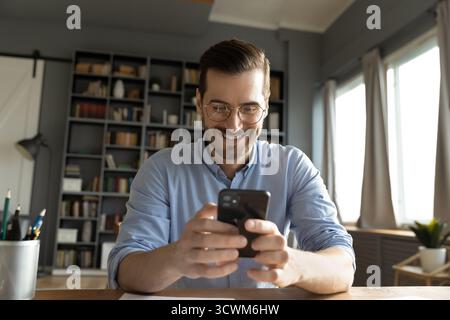 Cheerful young male checking smartphone app at home office desk Stock Photo