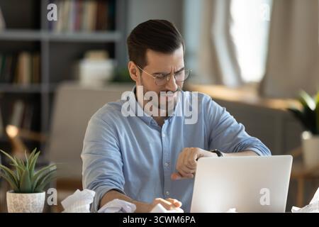 Nervous businessman checking wristwatch at office desk with crumpled documents Stock Photo