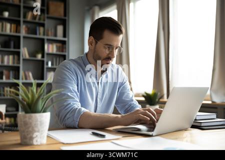 Focused millennial business specialist typing on notebook at workplace desk Stock Photo