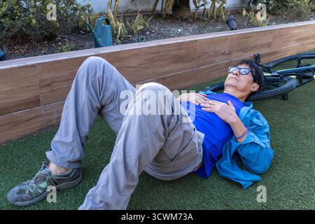 Man lying on artificial grass, hands on chest, relaxing near a fallen bicycle Stock Photo