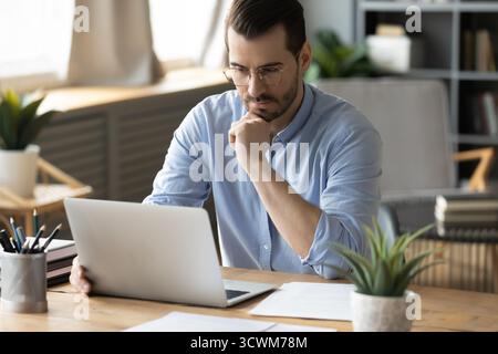 Pensive mid adult man office worker looking at notebook screen Stock Photo