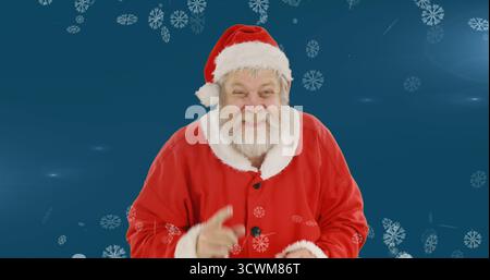Image of santa claus smiling over winter scenery with snow falling on blue background Stock Photo