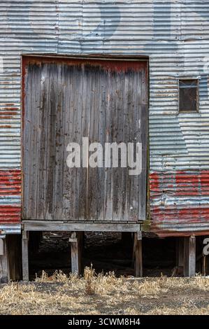 Weathered timber door set in a corrugated metal wall of an abandoned warehouse. The wood appears aged and worn, with visible stains and rough texture. Stock Photo