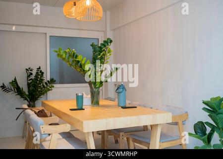 Modern minimalist dining room interior with wooden table, indoor plants, and warm pendant lights. Natural light, cozy chairs, and clean design create Stock Photo