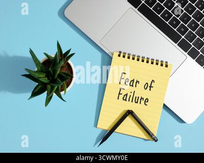 Yellow notepad with fear of failure message, broken pencil, laptop on blue background Stock Photo