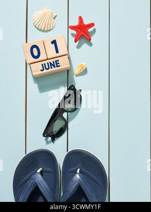 Flip-flops, sunglasses, seashells and starfish are celebrating the beginning of summer on a wooden background with a calendar showing June 1st Stock Photo
