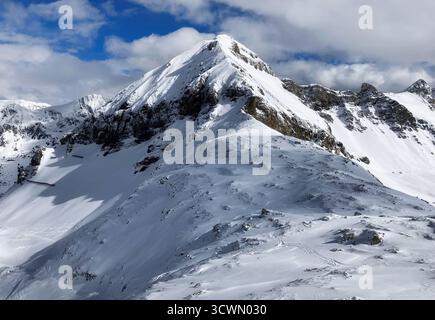 Skier standing on a snowy mountain slope with picturesque snow - capped peaks in the background under a blue sky with clouds. Austria - Obertauern Stock Photo