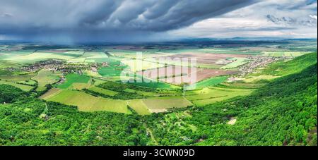 Summer storm clouds seen from a drone over a vast green forest and village with houses in a fairy tale landscape. Stock Photo