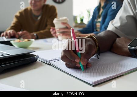 Multiethnic Team Collaborating and Taking Notes during Meeting Stock Photo
