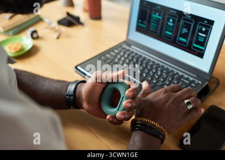 Black Man Using Hand Grip Exerciser While Working on Laptop Stock Photo
