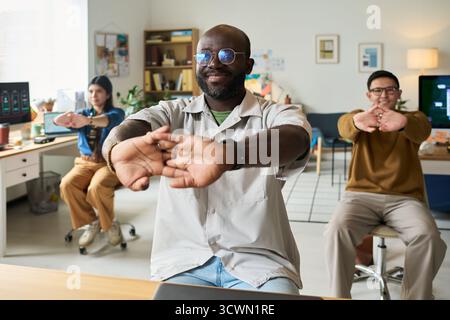 Black Man Leading Diverse Coworkers Stretching in Office Setting Stock Photo