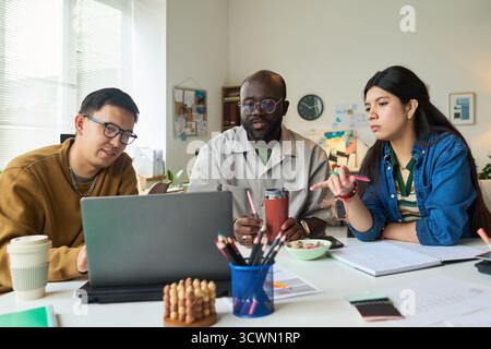 Multiethnic Adults Collaborating on Project Around Laptop in Office Stock Photo