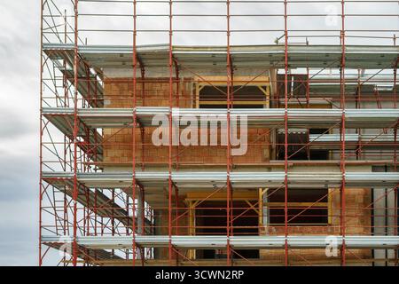 A modern brick structure surrounded by red scaffolding on an active construction site. Construction of a new building Stock Photo