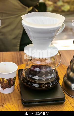 A barista prepares coffee using the pour-over method by pouring water into a funnel with a filter and coffee beans during a coffee festival. Stock Photo
