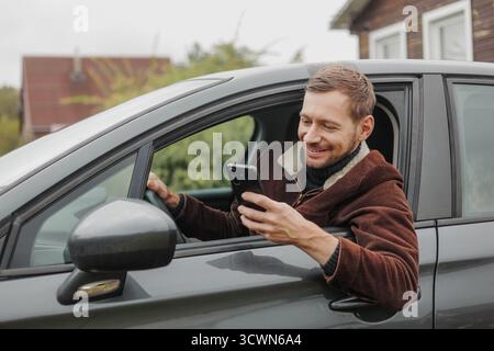 Smiling man driver in jacket using smartphone inside the car Stock Photo