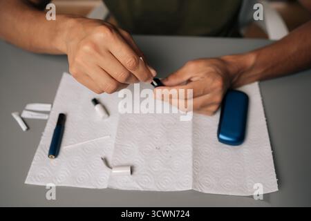 High-angle view of repairman cleaning electronic cigarette with cotton swab, focusing on proper maintenance and hygiene for vaping device sitting at Stock Photo