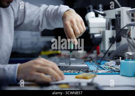A technician is carefully repairing a circuit board with precision tools in a workshop Stock Photo