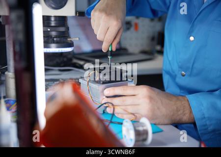 A technician is carefully repairing a circuit board with precision tools in a workshop Stock Photo