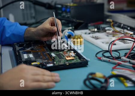 A man works on his laptop while using a soldering iron Stock Photo