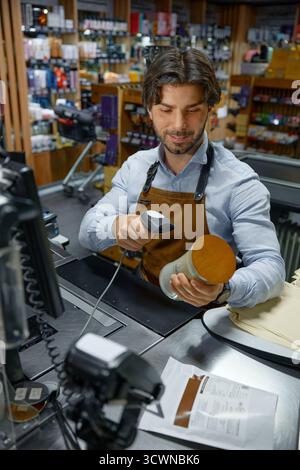 A man cashier wearing an apron is actively using a barcode scanner to scan a candle Stock Photo