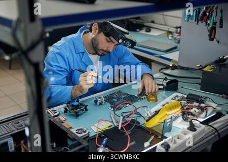 A man soldering technician is fully focused on working on a computer Stock Photo