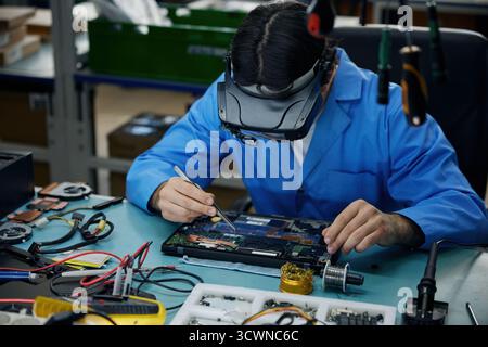 A man soldering technician dressed in a blue lab coat is diligently repairing a laptop Stock Photo