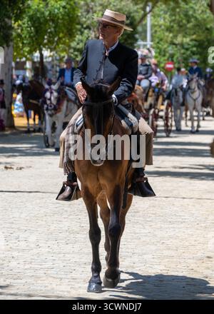 Sevilla, Spain - 23 Apr 23: A man in a black suit and hat riding a horse during a festive event, surrounded by other riders and spectators Stock Photo