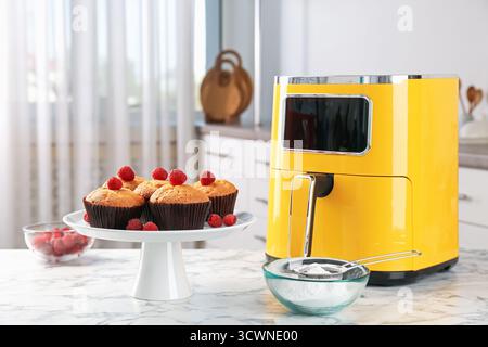 Freshly baked muffins with raspberries, flour and air fryer on white marble table in kitchen Stock Photo