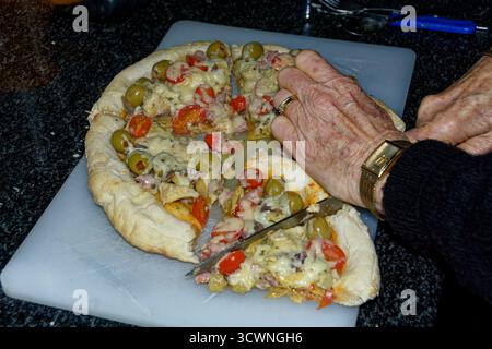 Pizza - a Margherita base with additional ingredients added being sliced for serving. Stock Photo
