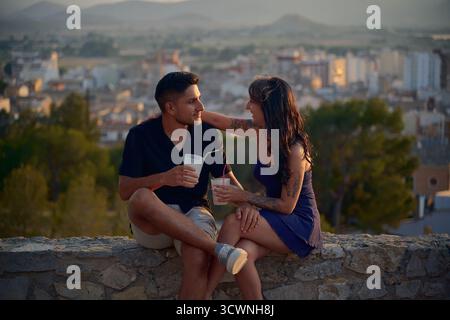 Young couple enjoying drinks on city view terrace at sunset Stock Photo