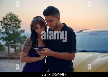 Young couple using smartphone together during sunset trip Stock Photo